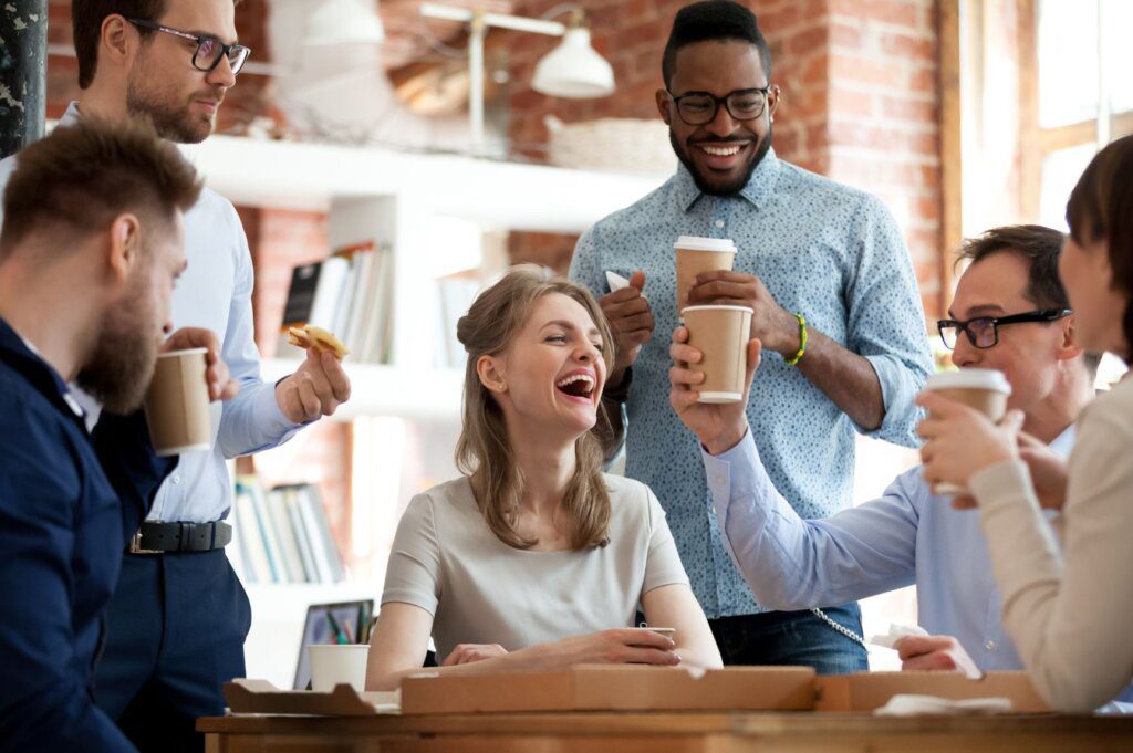 Coworkers laughing together with cups of coffee.