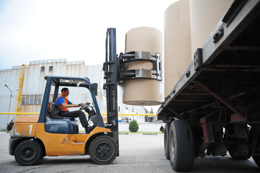 Clamping forklift in action at a warehouse, using a clamp truck attachment to securely handle large paper rolls