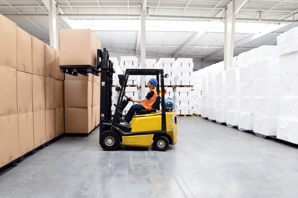 Slip sheet forklift attachment in use, optimizing material handling and space efficiency in a warehouse.
