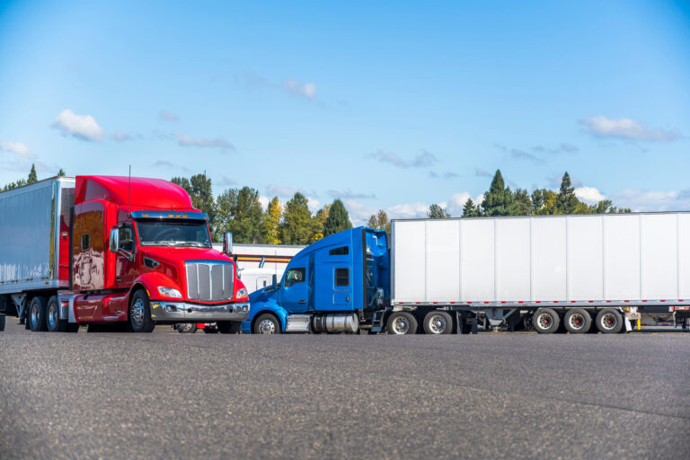 Red and blue semi-trucks parked at a logistics hub, representing full truckload and LTL freight shipping operations.