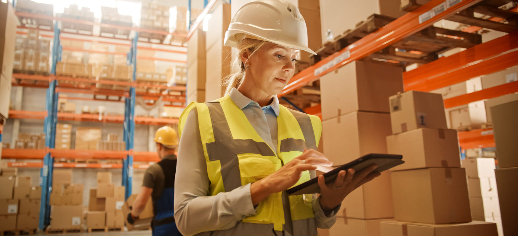 Worker in commercial warehouse checking inventory on tablet.