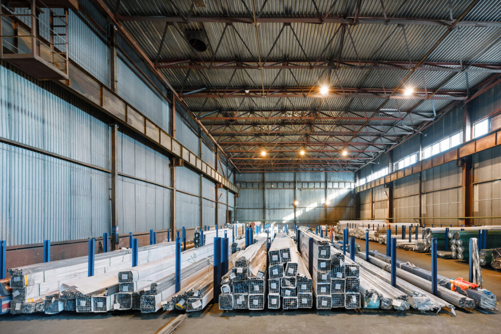 Interior of a large industrial warehouse with high ceilings, pallet racks and forklifts moving goods.