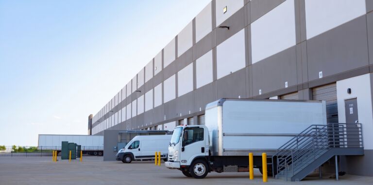 Modern distribution center with docked box truck, cargo van, and loading bays.